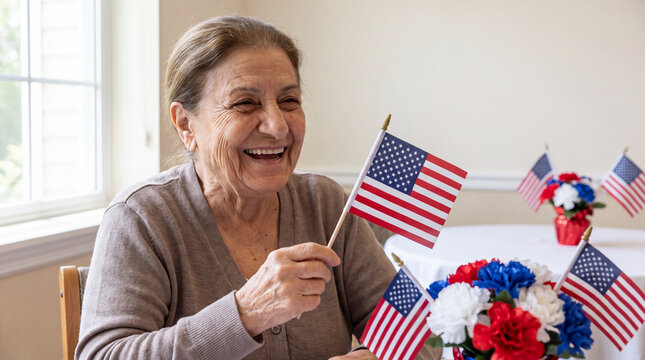 A grateful elderly Middle Eastern female veteran laughs while holding an American flag in a nursing home dining area with patriotic decor for senior living websites.