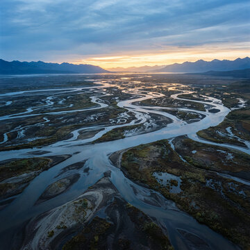 Braided river channels wind across a flat valley beneath a colorful sunset sky