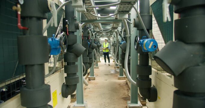An engineer in a hard hat inspects the complex piping of an industrial HVAC system, conducting a quality control check on the facility's heating and cooling infrastructure.