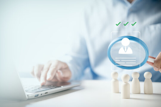 HR manager using magnifying glass to select candidate profile over wooden figures on desk, concept of talent acquisition, recruitment, human resources management, and hiring process.