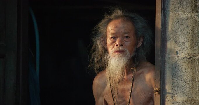 A rural senior man with a long white beard steps to an open door, gazing out at the last light of dusk before sunset.