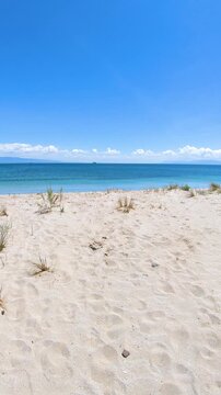 Vertical POV walk along a sandy path toward Mare Morto beach in Sardinia, capturing the quiet Mediterranean coast and an empty shoreline with no people.