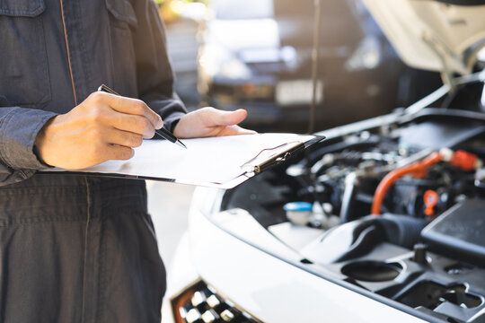 Auto check, car service shop concept. Automobile repairman writing job checklist on clipboard, mechanic checking engine to estimate repair machine, inspecting maintenance by engineer at vehicle garage