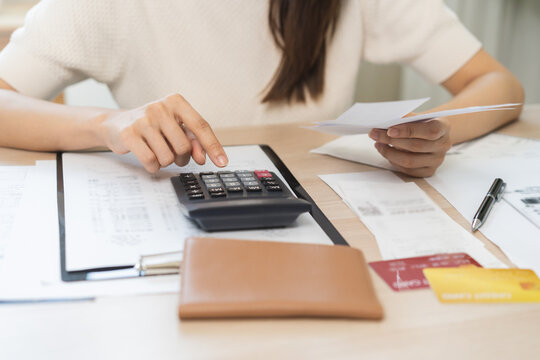Stressed asian young business woman, employee using calculator to calculate expenses of monthly, hand holding bills and receipt for to payment on table at home. Financial, finance of banking concept.