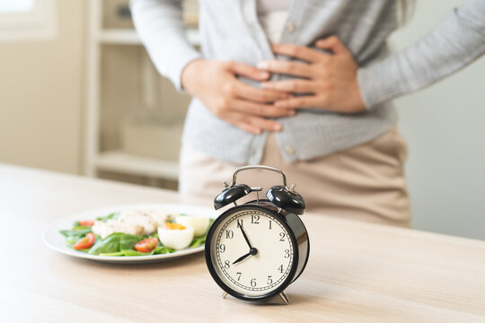 Intermittent fasting, diet healthy asian young woman dietary, having stomach ache, temptation hungry of brunch food in morning on table at home, waiting time to eat salad but not yet time first meal.