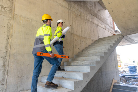 Male and female engineers walking up concrete stairs carrying tools