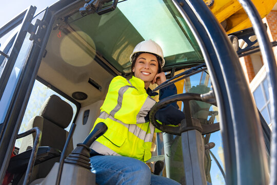 Happy female heavy equipment operator smiling inside excavator cabin