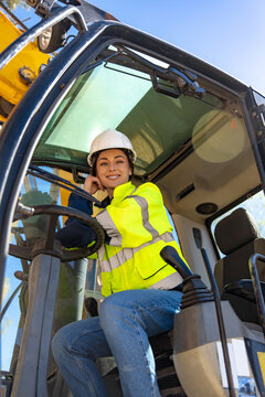 Cheerful female driver sitting in excavator cabin and smiling