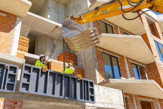 Builders attaching heavy metal panel to excavator chains
