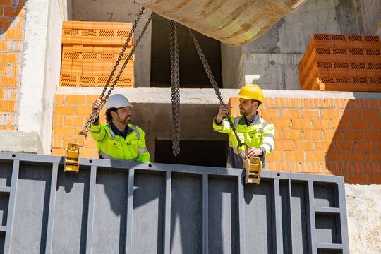 Two male builders adjusting chains on steel formwork panel