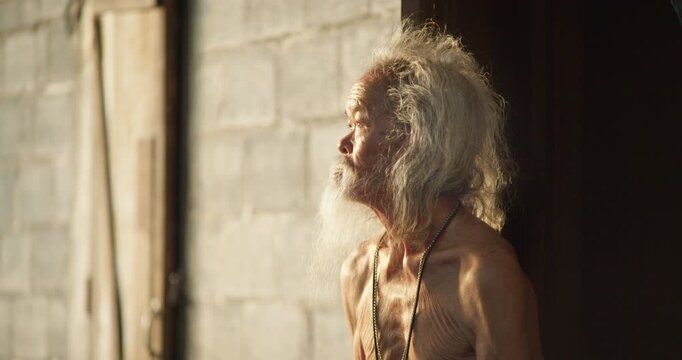 A rural senior man with a long white beard steps to an open door, gazing out at the last light of dusk before sunset.