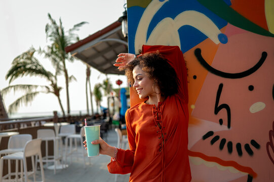 Beautiful young woman smiles warmly in a vibrant portrait against colorful street art on a sunny day