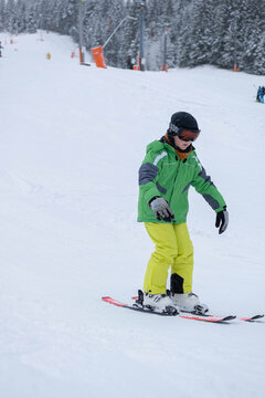 A boy makes his first attempts at skiing on a snowy slope at a winter resort. The scene represents ski learning, childhood activity, and a first winter sports experience.