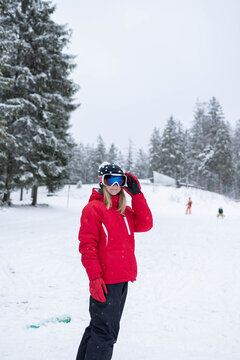 A young girl adjusts her goggles while standing on skis at a snowy winter resort. The scene represents ski preparation, youth activity, and winter sports learning.