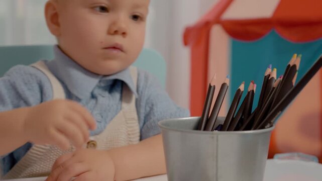 A young boy is eager to assist his mother in sharpening colored pencils. Together, they enjoy a fun and creative moment in their sunny kitchen.