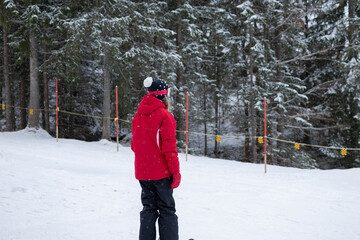 A young girl stands on skis and looks across a snowy slope surrounded by forest at a winter resort. The scene represents youth skiing, winter recreation, and outdoor adventure. © Liudmila