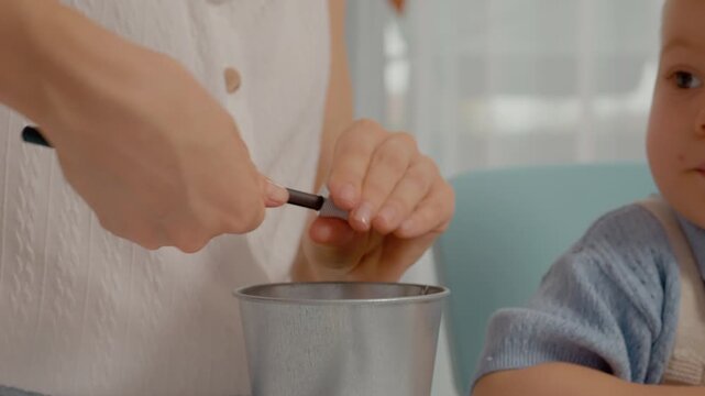 A little boy joyfully helps his mother sharpen colored pencils at their home. The colorful pencils are scattered around as they work together in a creative space.