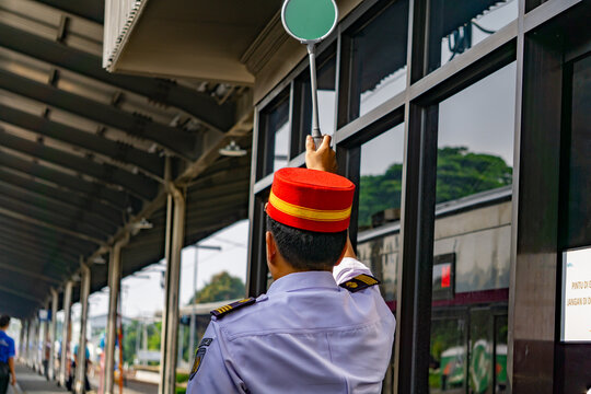 A station master complete with his uniform and red hat is holding up the green sign indicating that the train is allowed to depart
