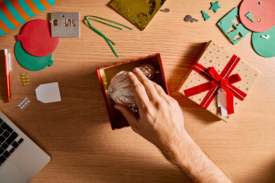 Overhead View of Man Packing Christmas Baubles in Gift Box on Wooden Desk