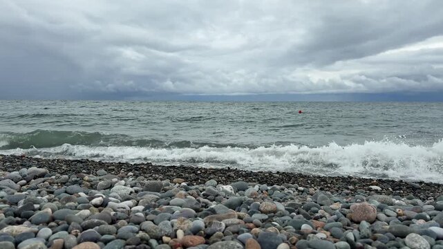  Sea waves breaking with white foam on pebble beach coastline under atmospheric overcast cloudscape sky, real time video