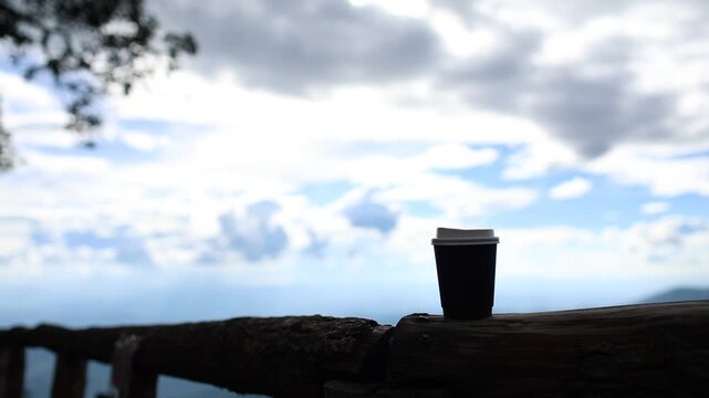 Black Coffee Cup on a Wooden Bench with Dramatic Mountain and Cloudy Sky