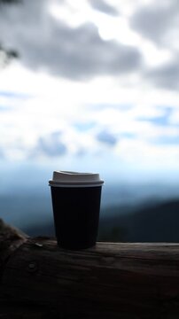 Black Coffee Cup on a Wooden Bench with Dramatic Mountain and Cloudy Sky