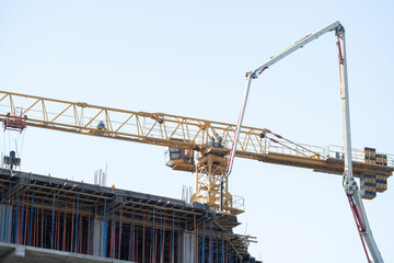 Yellow tower crane and concrete pump arm working at high rise building construction site under blue sky © Сергей Дудиков