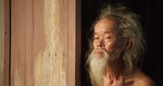 A rural senior man with a long white beard steps to an open door, gazing out at the last light of dusk before sunset.