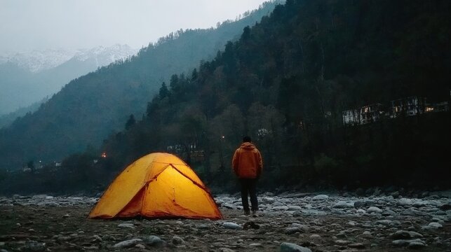 Man Standing By Illuminated Tent In Mountain Wilderness