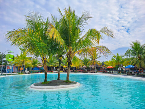 Turquoise swimming pool with coconut palm trees on a small island, perfect tropical vacation and summer holiday destination background.