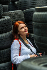 woman with red hair stands with  camera on background of car tires, leaning back, holding in her hands, black rubber, portrait,  © Studio  GULL