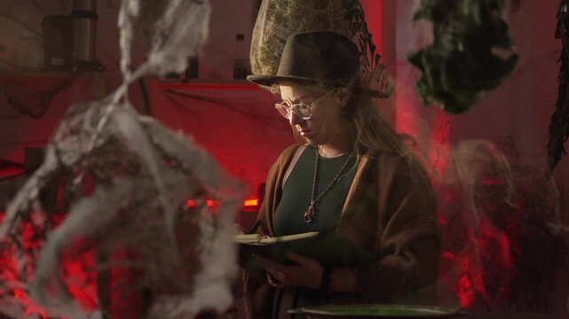 A realistic witch brewing a potion. She s looking into the cauldron and reading a spell from a notebook. Everyday life and traditional witchcraft. Magic and a mystical atmosphere.