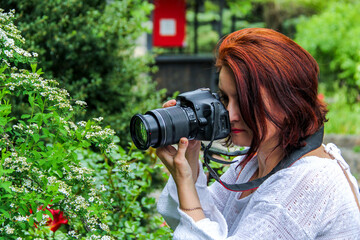 woman with red hair holds black digital camera near eye, profile, portrait, SLR, mirrorless, middle age © Studio  GULL