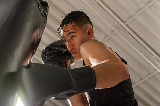 Hispanic boxer striking heavy bag from low angle during training