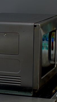 vertical close-up of dark gray metal appliance side front corner, access hatch closed and stainless door with tubular handle, indoor lighting detail inside sun