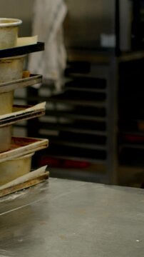 close-up vertical view of stacked cylindrical baking pans and metal trays on rack above scratched tabletop in commercial kitchen or bakery preparation area tray