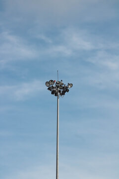 High mast floodlight tower with array of lamps against blue sky