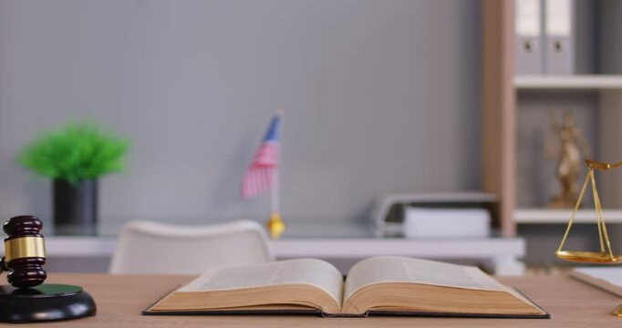 Close up of judge's workplace with gavel and scales with USA flag in background. Empty interior of courtroom or lawyer office. Jurisdiction, legal law and justice concept. 4k video. 