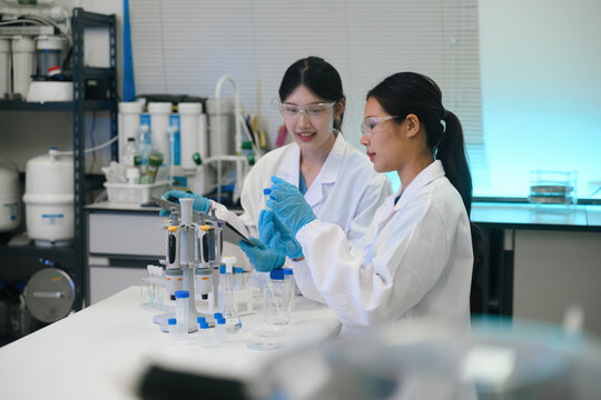 Two Asian Female Scientists Working Together in Modern Laboratory with Pipettes and Test Tubes