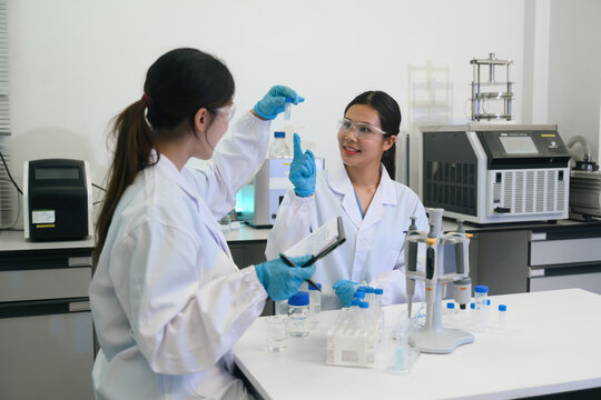 Two Female Asian Scientists Collaborating in Modern Laboratory While Examining Test Tube Sample