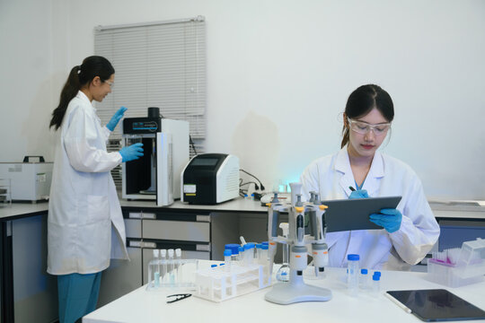 Two Asian Female Scientists Working in Modern Medical Research Laboratory with Equipment and Digital Tablet