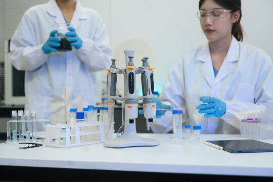 Two Asian Scientists Working Together in Modern Research Laboratory with Pipettes and Test Tubes