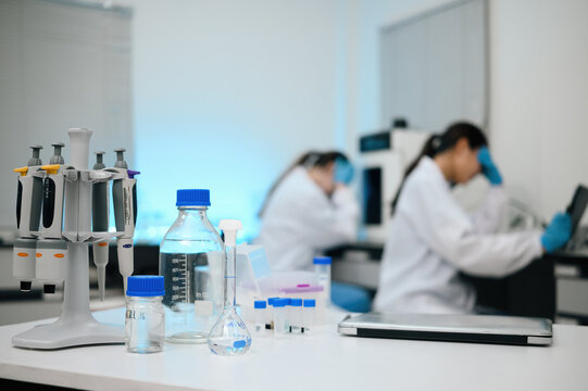 Female Scientists Working in Modern Research Laboratory with Pipettes and Glassware in Foreground