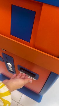 Vertical 4K video. Woman puts paper purple banknote one hundred lari into orange blue ATM with symbol of Georgian currency. 100 GEL in female hand. Concept of cash money, salary, tax, loan, bribe