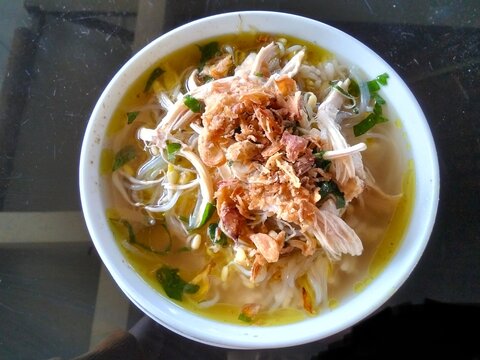 Traditional Indonesian chicken soup called soto ayam served in a white bowl with vermicelli, shredded chicken, bean sprouts, and fried shallots.