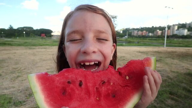 Happy child girl eating watermelon fresh fruit at park city - Summer vacation concept