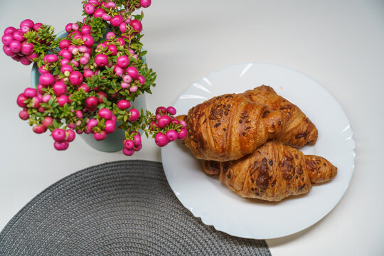 Golden chocolate croissants arranged on a white plate beside a decorative Pernettya mucronata (Gaultheria mucronata) plant with abundant bright pink berries