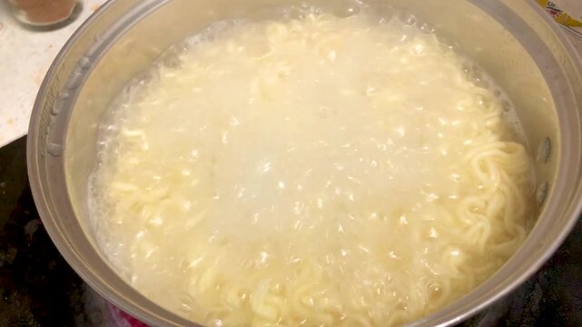 Instant ramen noodles boil in a pot during home cooking.