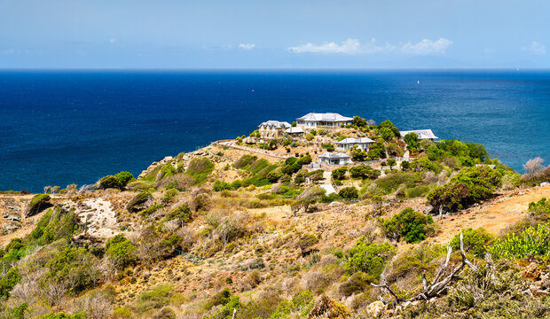 Coastal villas and houses on a sunny green hilltop overlooking Windward Bay and the deep blue ocean in Antigua and Barbuda.