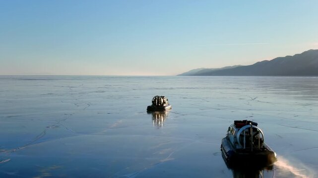 Hovercrafts moving over thin ice on frozen Baikal lake. Amphibious vehicle sliding, winter transport. Arctic transportation, extreme travel exploration in cold climate landscape. Mountains background.